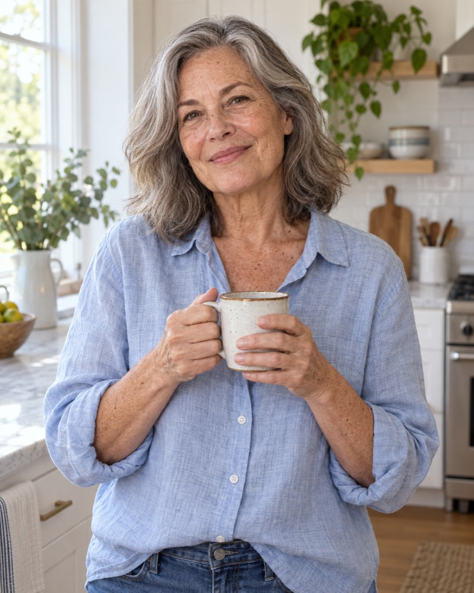 Smiling woman in her 60s holding a coffee mug in morning light